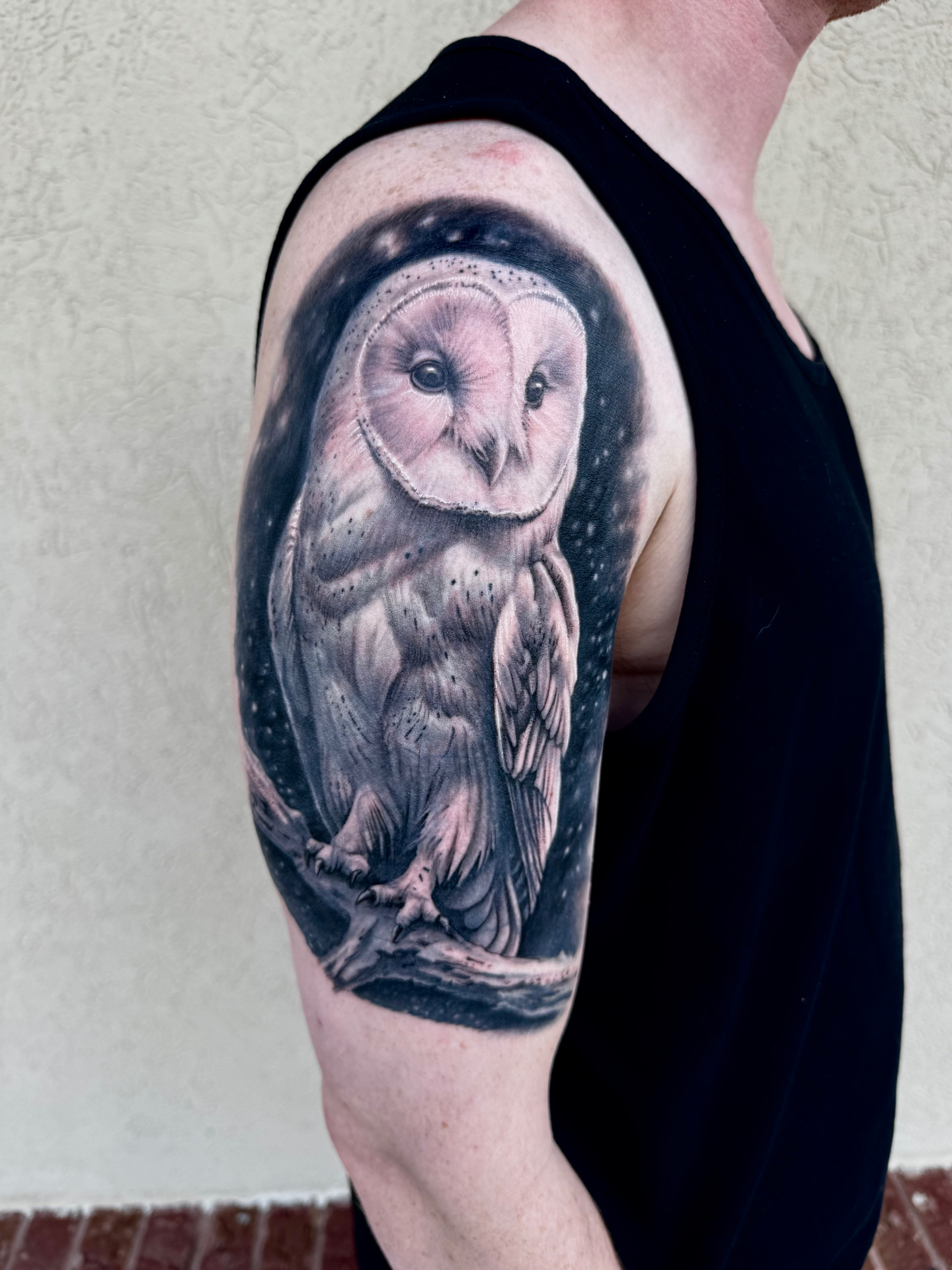 Large black and grey owl tattoo covering the upper arm and shoulder