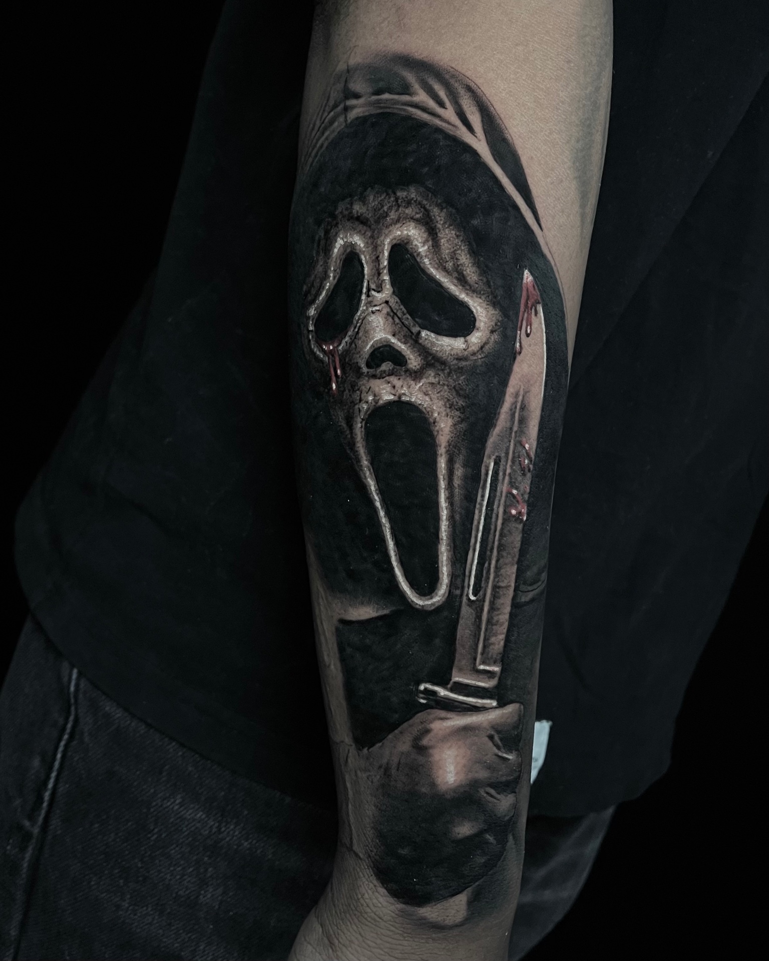Black and grey Ghostface tattoo holding a knife on the forearm